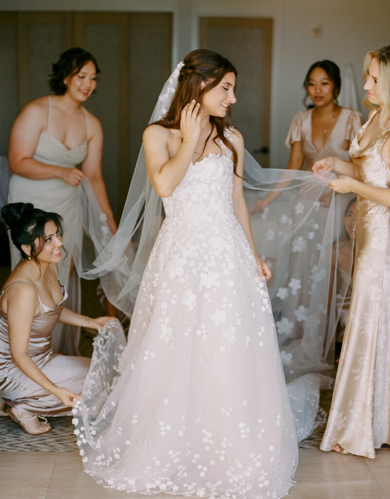 Bride smiles as bridesmaids arrange her gown.