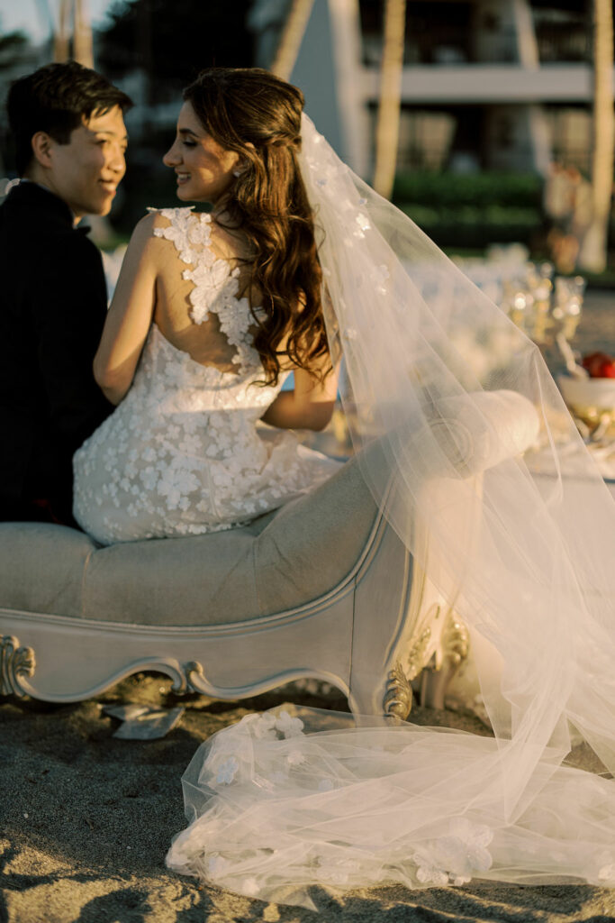 Bride and groom on chaise in golden sunlight.