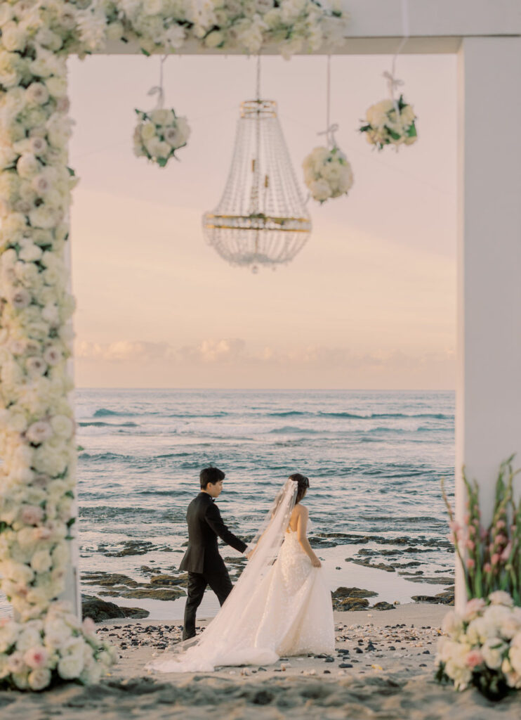 Bride and groom under floral arch at sunset.