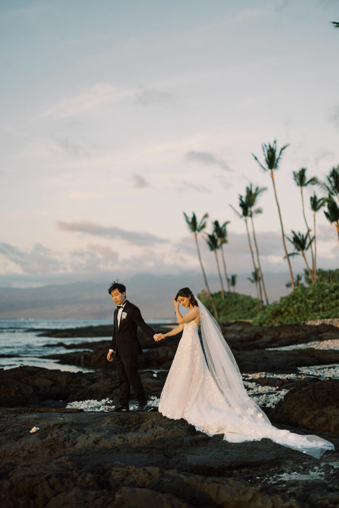 Bride and groom walk on beach at sunset.