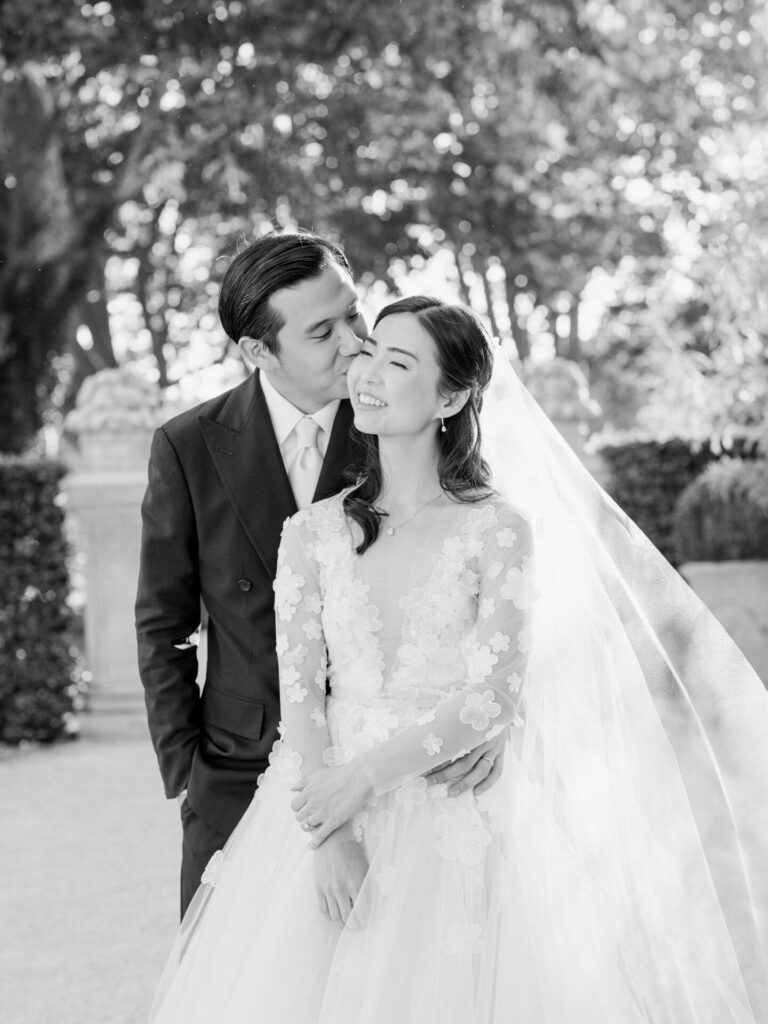 Groom kisses smiling bride in floral dress.