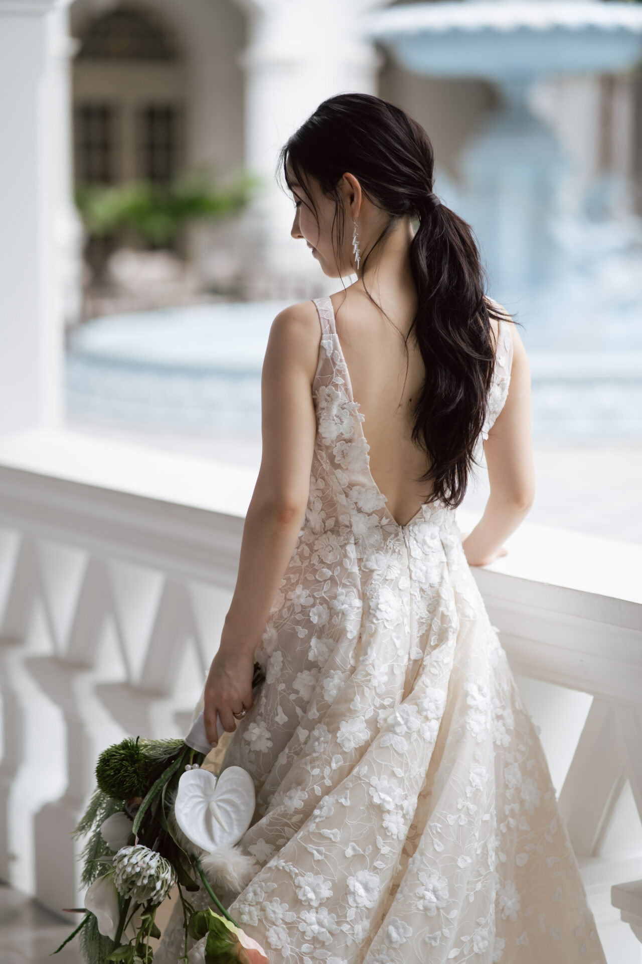 Woman in lace dress holds bouquet, facing away.