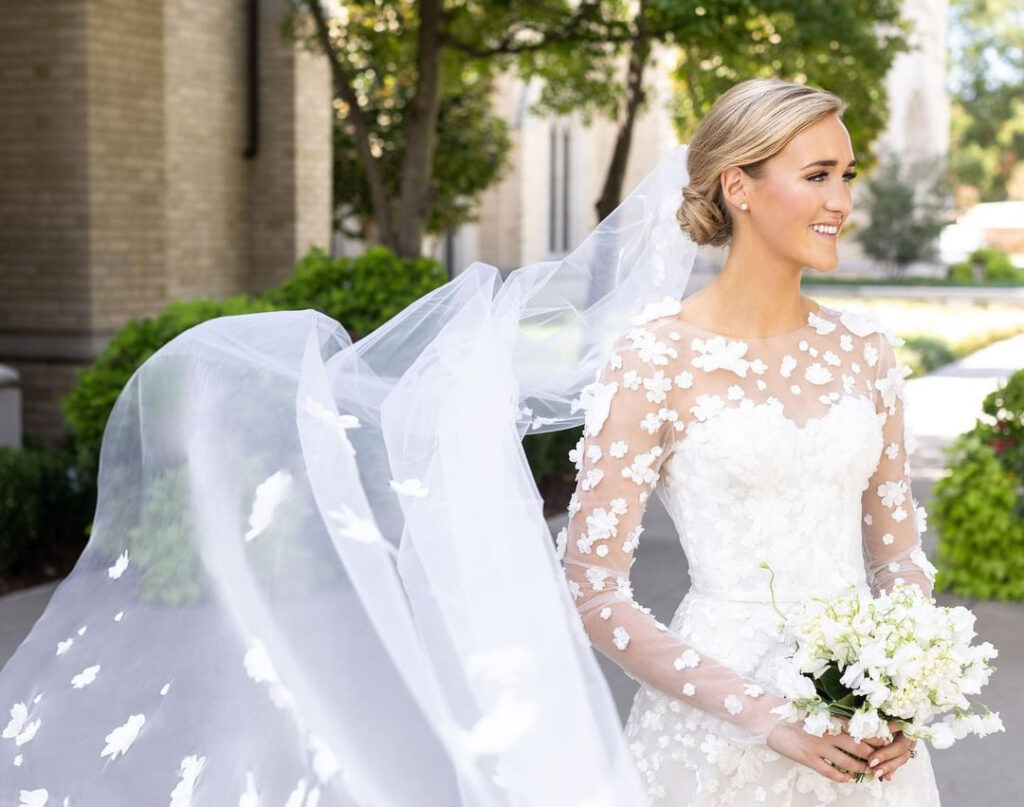 Bride in floral dress and veil holding bouquet.