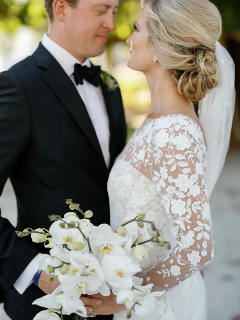 Bride and groom smiling outdoors, holding bouquet.
