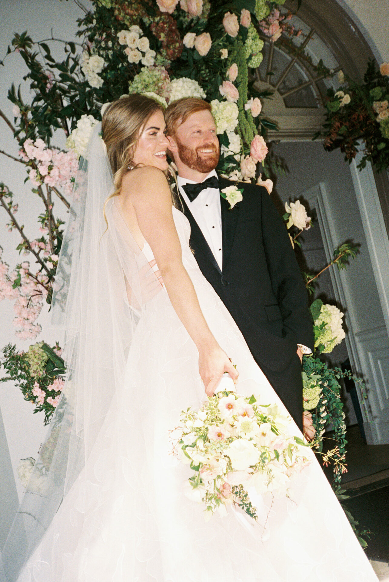Bride and groom posing with bouquet, flowers.