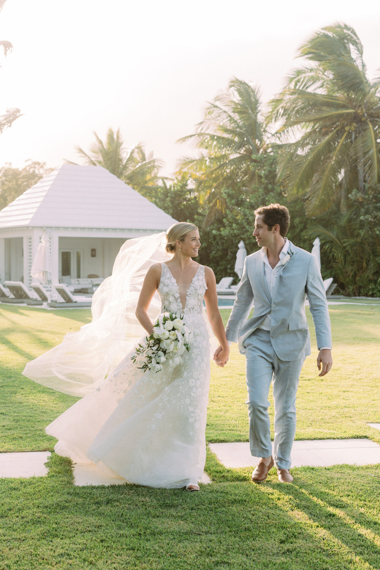 Bride and groom walk on sunny lawn.