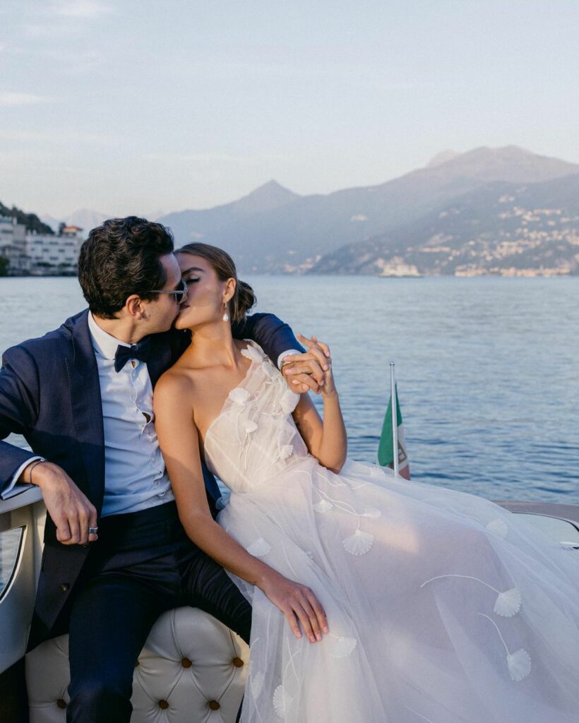 Couple kisses on boat, Italian flag, mountains.