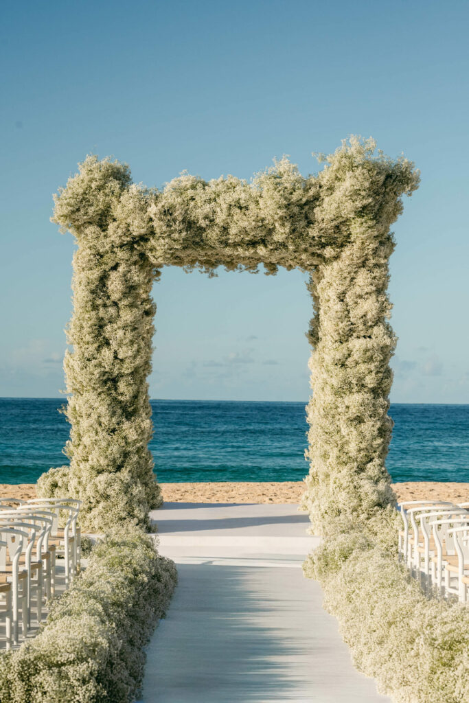 Bride Katya Ruiz under floral arch on beach.