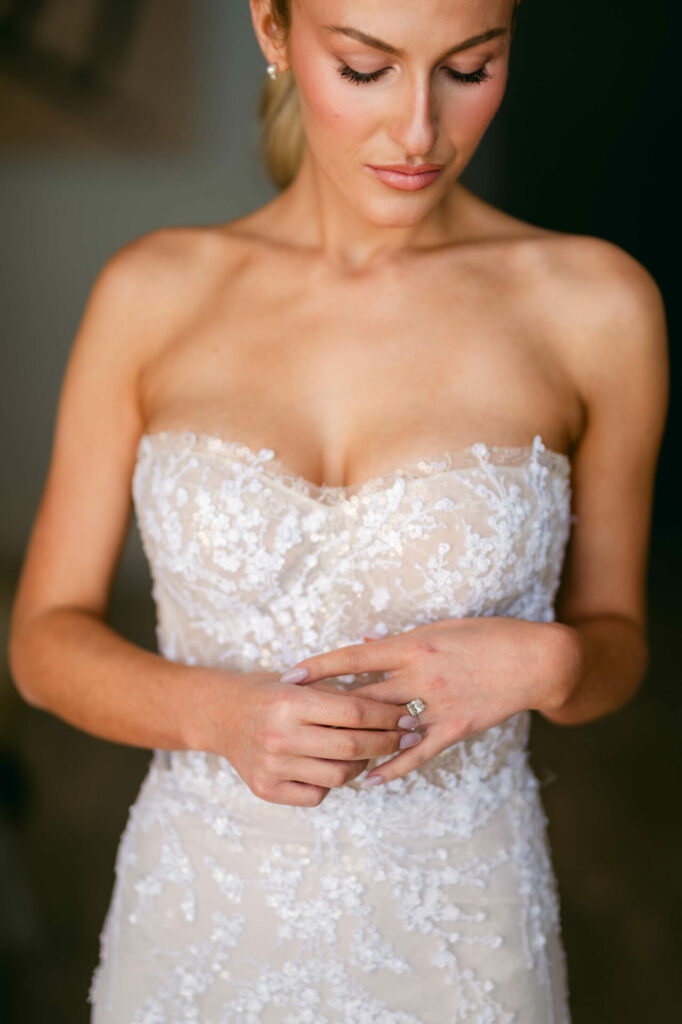 Woman in lace gown shows engagement ring.