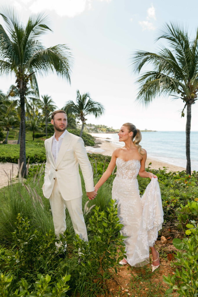 Bride and groom holding hands by beach.