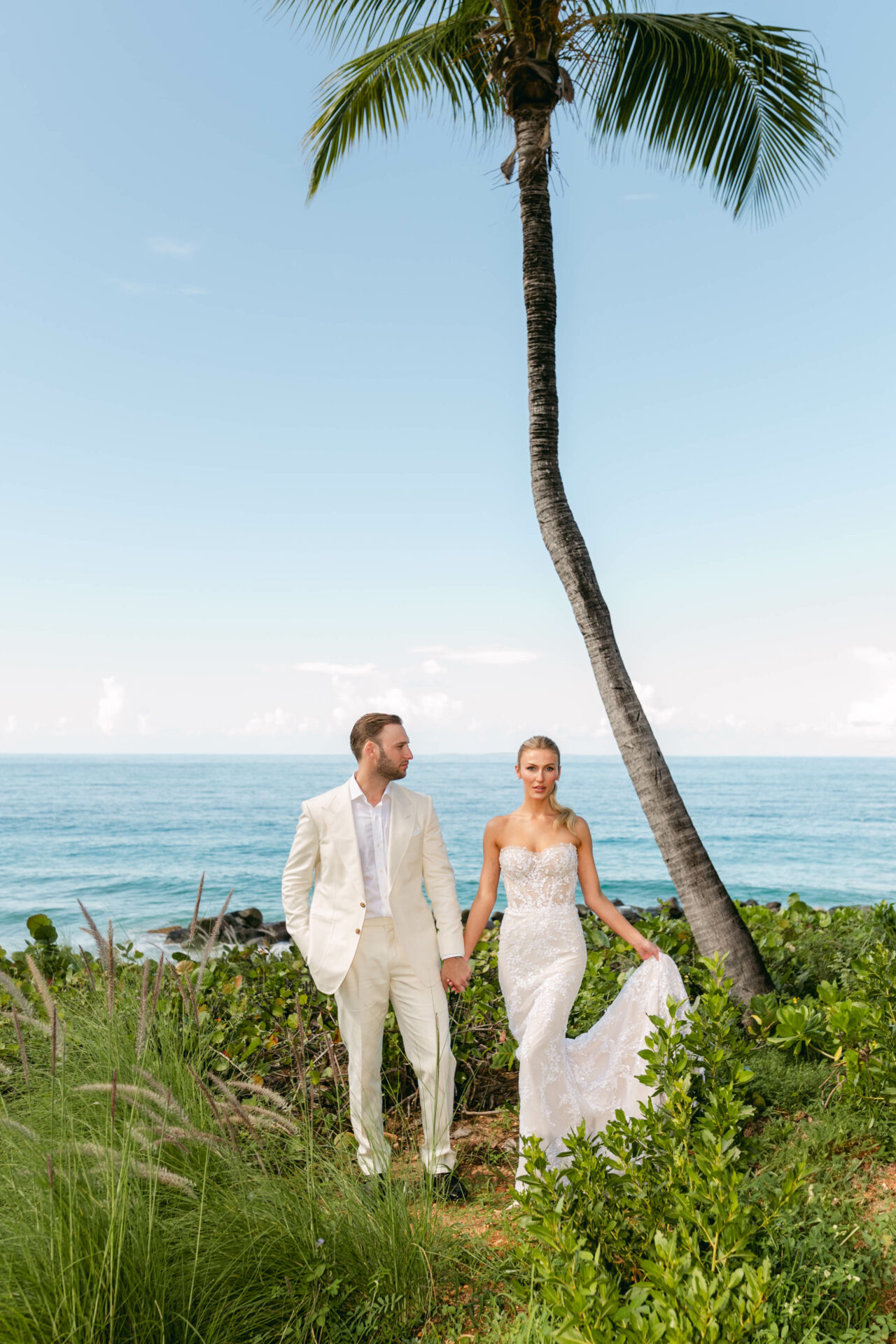 Bride and groom by ocean in white attire.