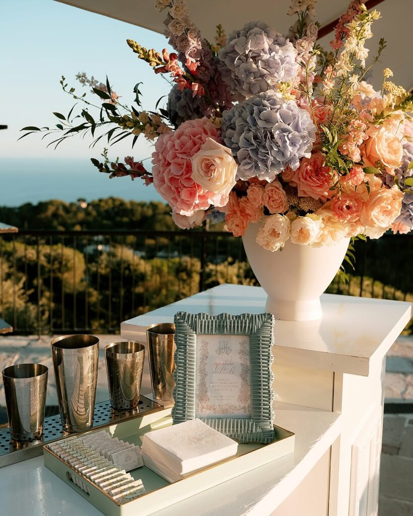 Outdoor table with flowers, cups, and ocean view.
