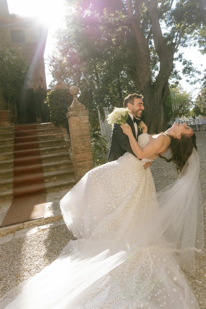 Groom dips bride in playful outdoor dance.