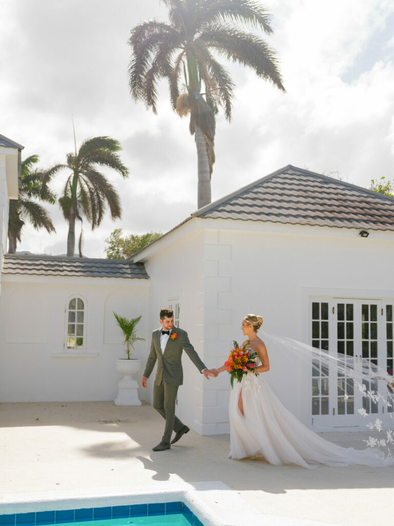 Bride and groom by pool, villa, palm trees.