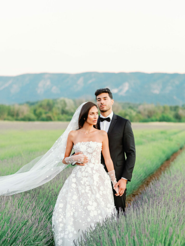 Bride and groom hold hands in lavender field.