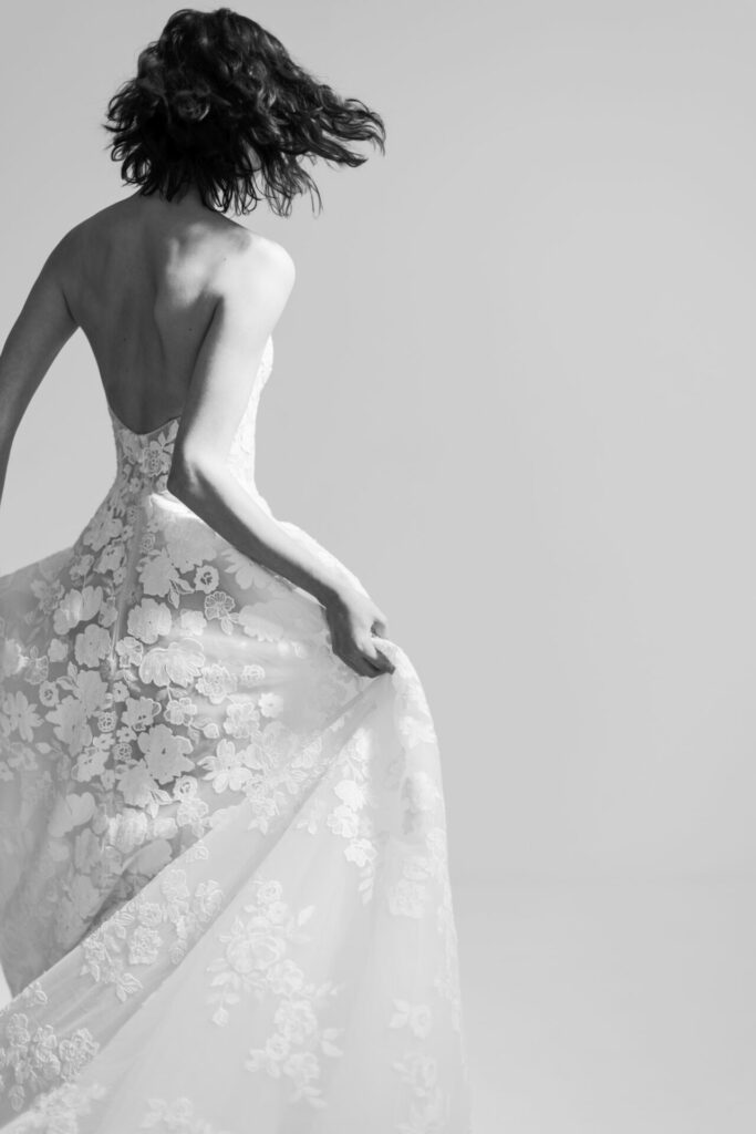 Woman twirling in strapless lace gown, rear view.