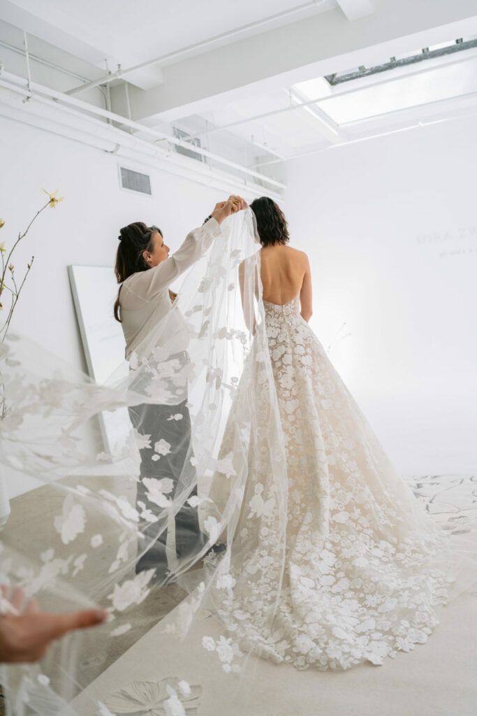 Woman in floral wedding gown, veil adjusted.
