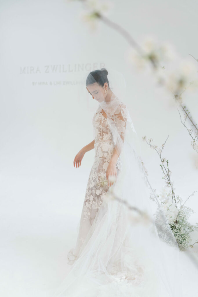 Bride in floral lace dress amidst blossoms.
