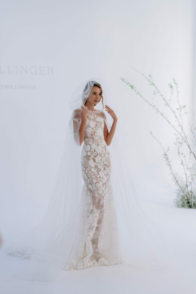Bride in lace gown poses by greenery.