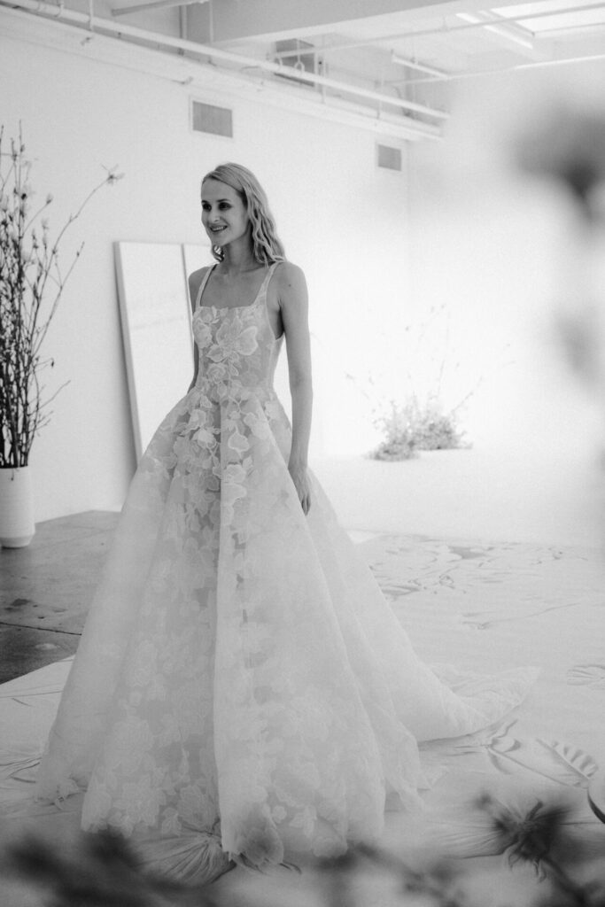 Woman in floral gown stands in sunlit room.
