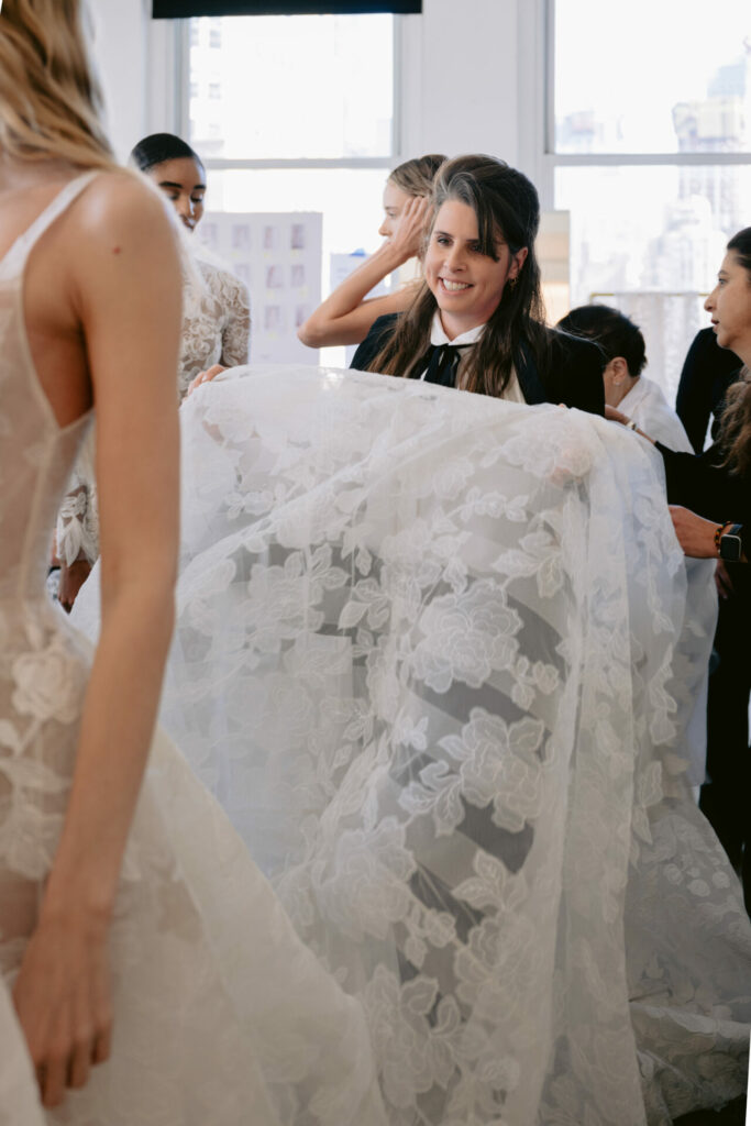Woman holds sheer white lace gown, smiling.