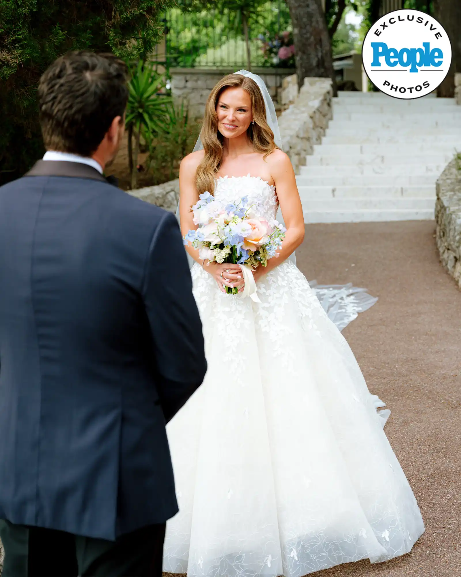 Bride smiles at groom outdoors, People logo.