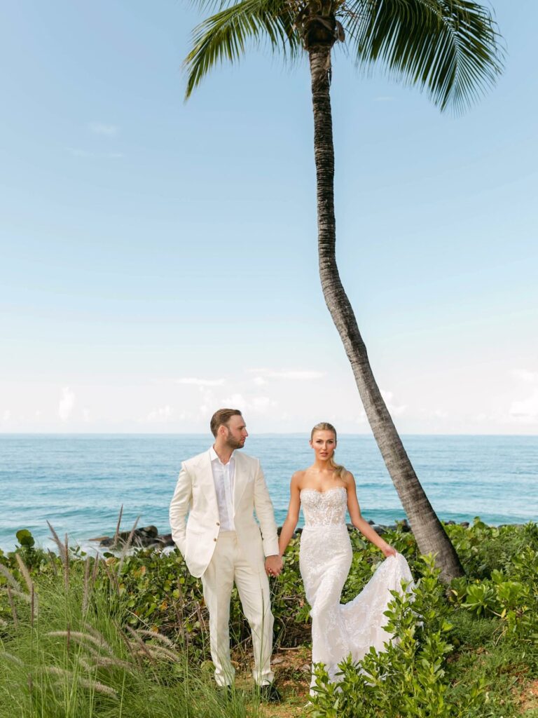 Bride and groom hold hands by palm tree.