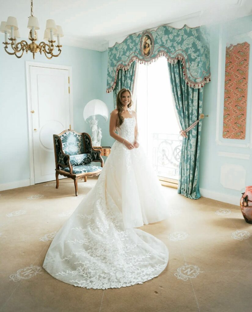 Bride smiles by window in elegant blue room.