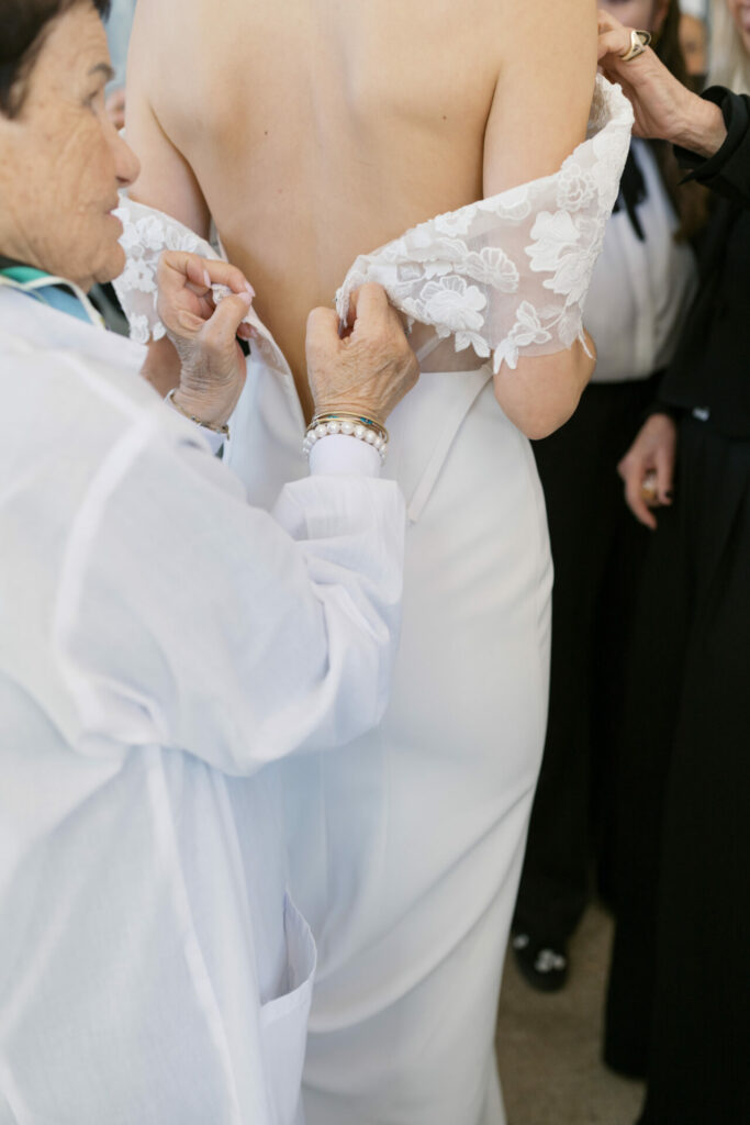 Older woman adjusts bride’s lace wedding sleeve.