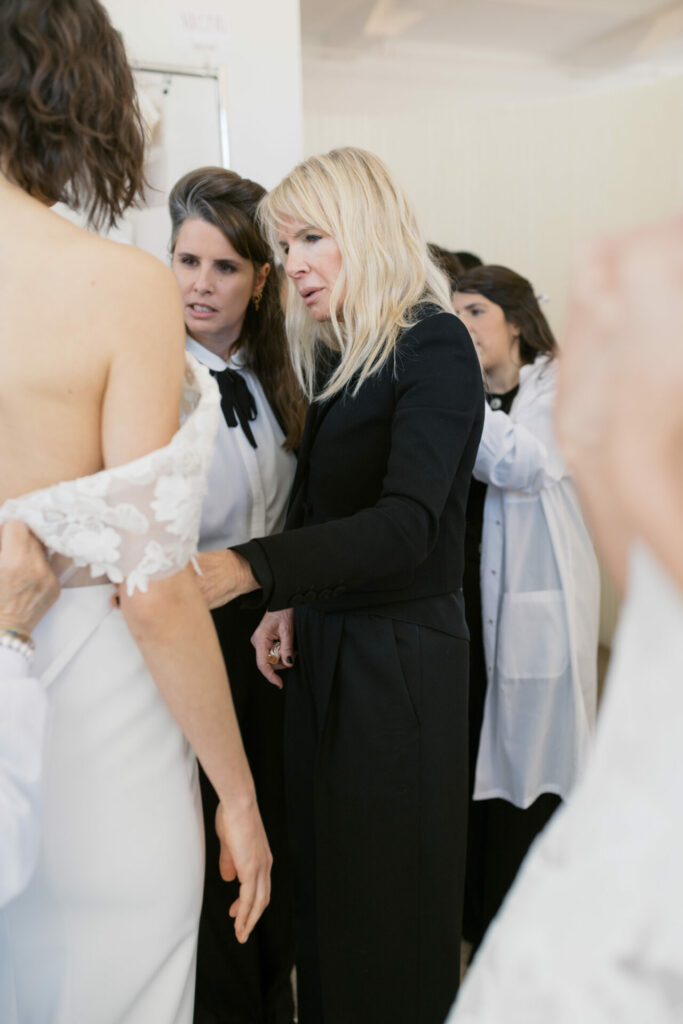 Woman adjusting bride’s lace sleeve indoors.