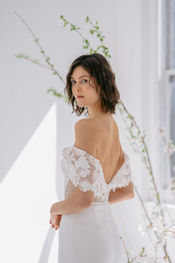 Bride in lace dress looks over shoulder.