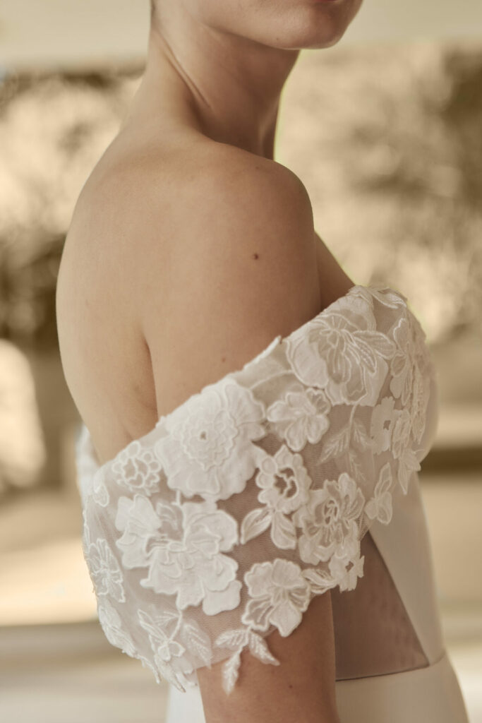 Woman in off-shoulder lace dress, blurred background.