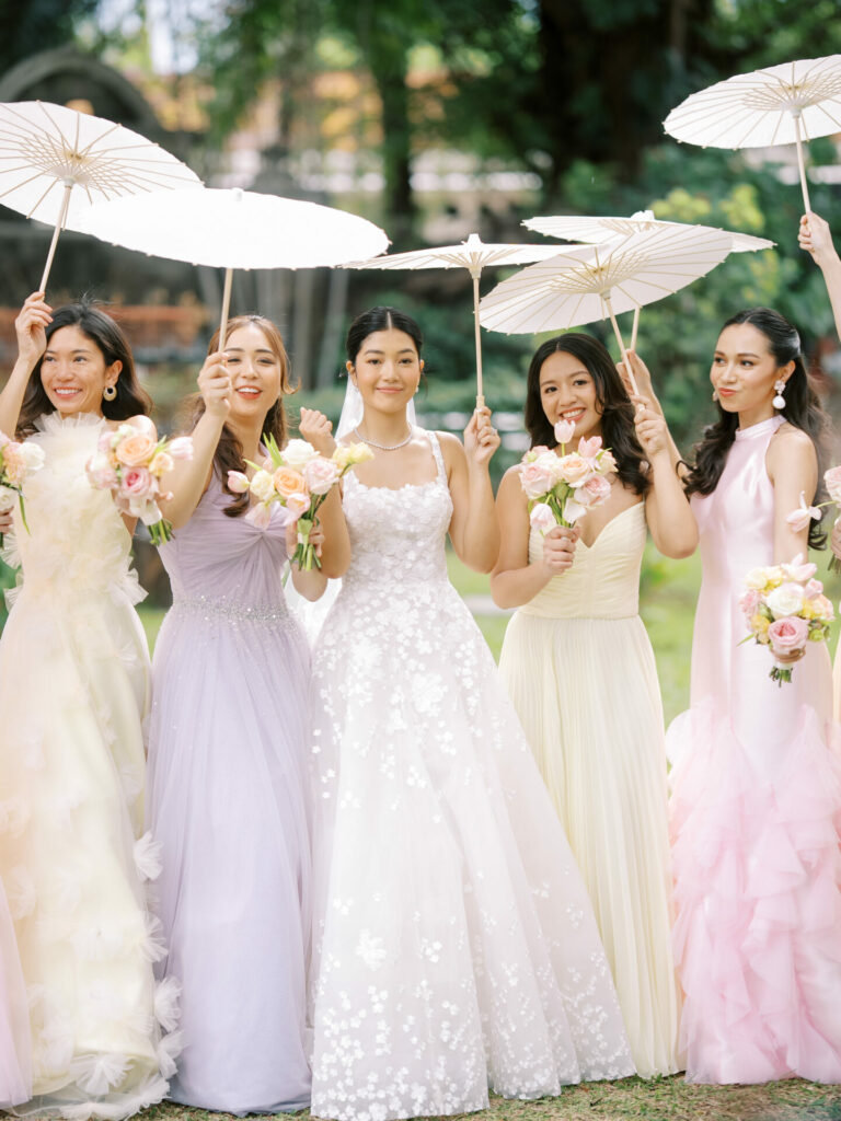 Bride and bridesmaids smiling with parasols outdoors.