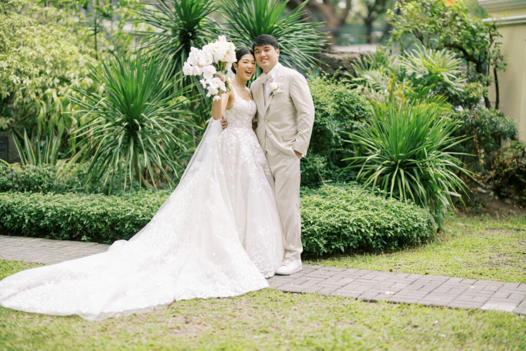 Bride and groom in garden, smiling elegantly.