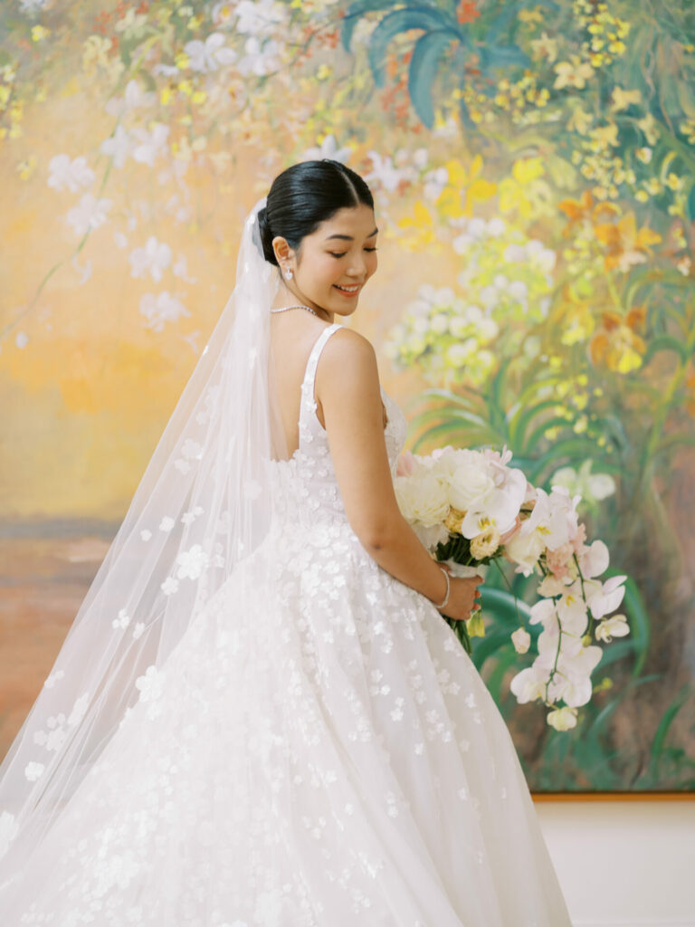 Bride in couture gown holding bouquet, smiling.