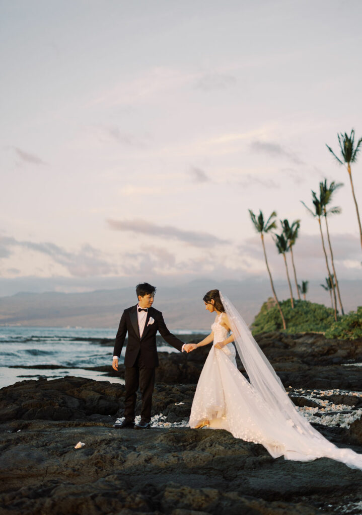 Bride and groom on rocky sunset shore.