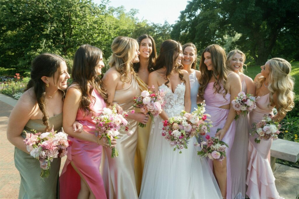 Bride and bridesmaids laughing outdoors with bouquets.