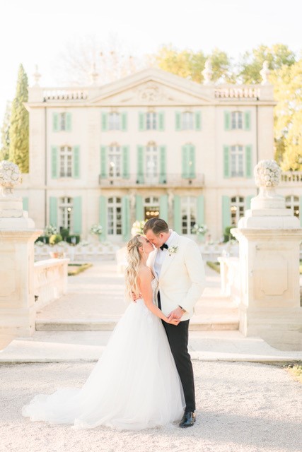 Bride and groom kiss outside elegant mansion.