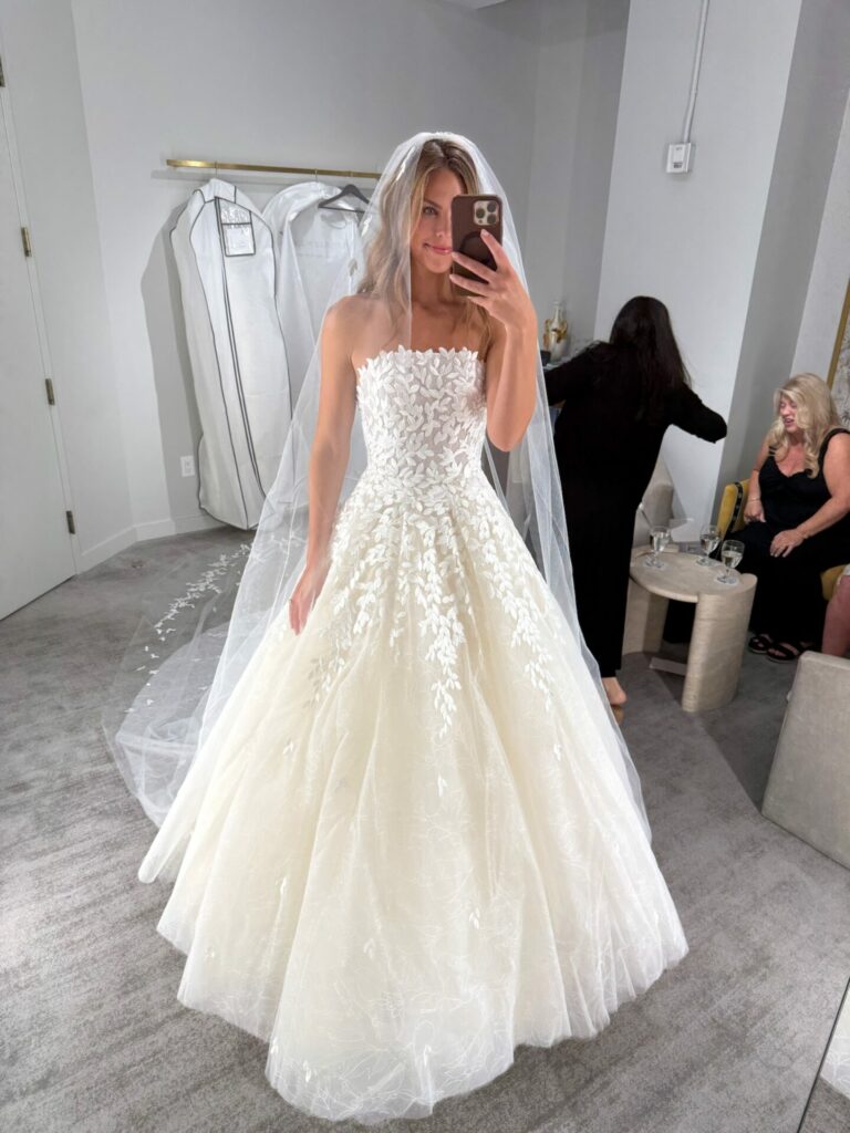 Bride takes mirror selfie in fitting room.