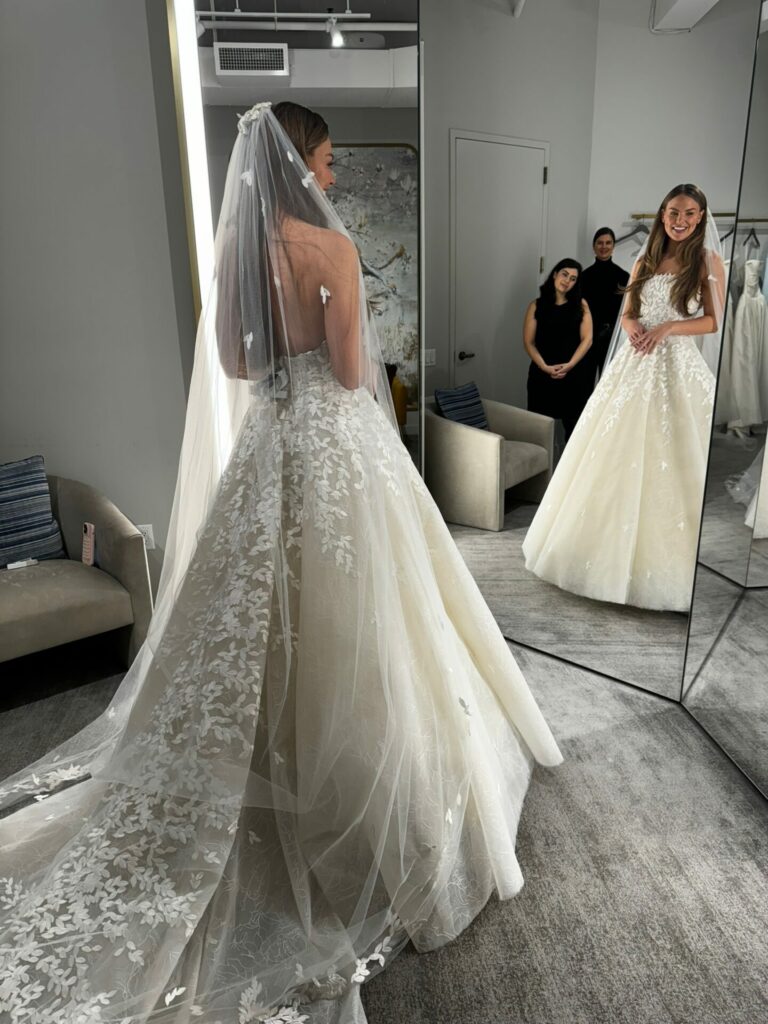 Bride smiling in mirror, two people behind.