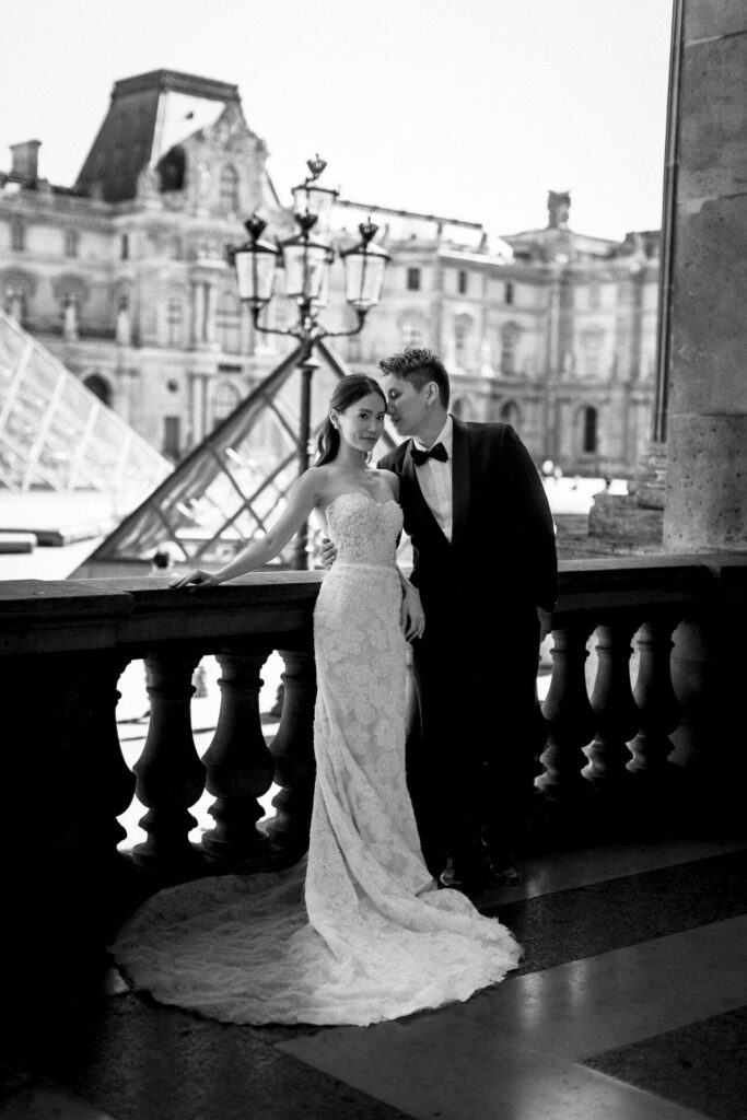 Bride and groom, Louvre backdrop, wedding attire.