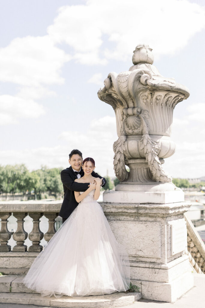 Bride and groom embrace on terrace, smiling.