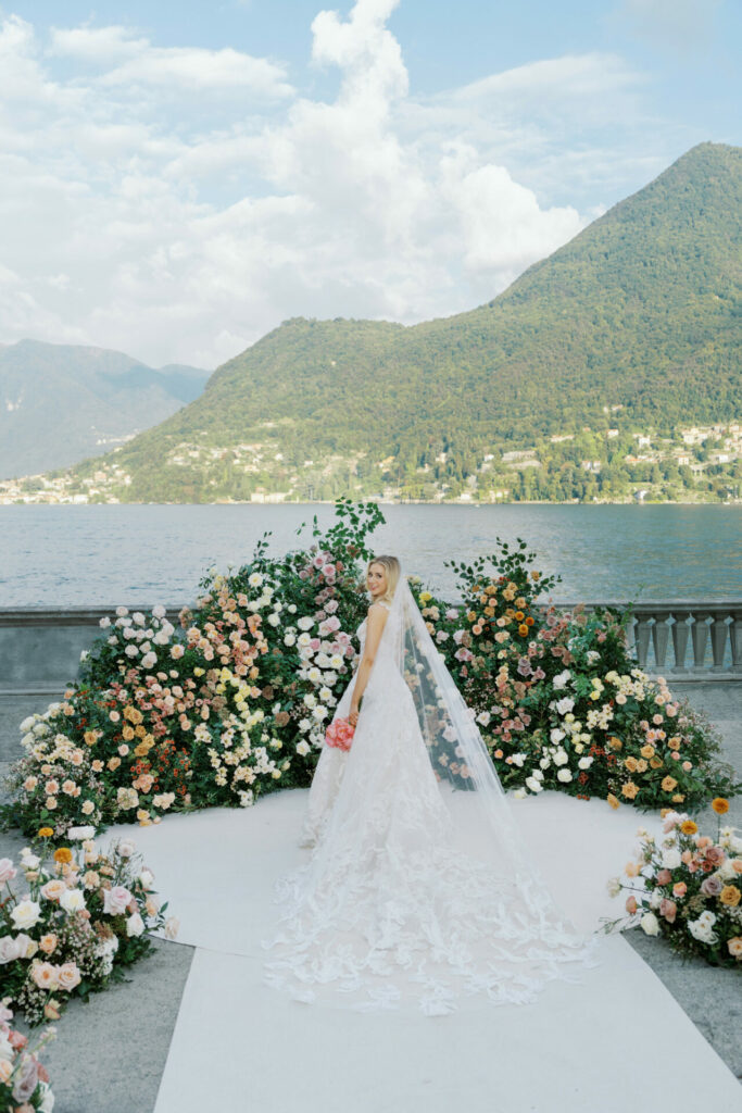 Bride on aisle, flowers, lake and mountains.