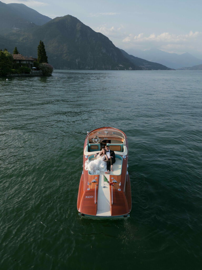 Bride and groom on boat amid scenic lake.