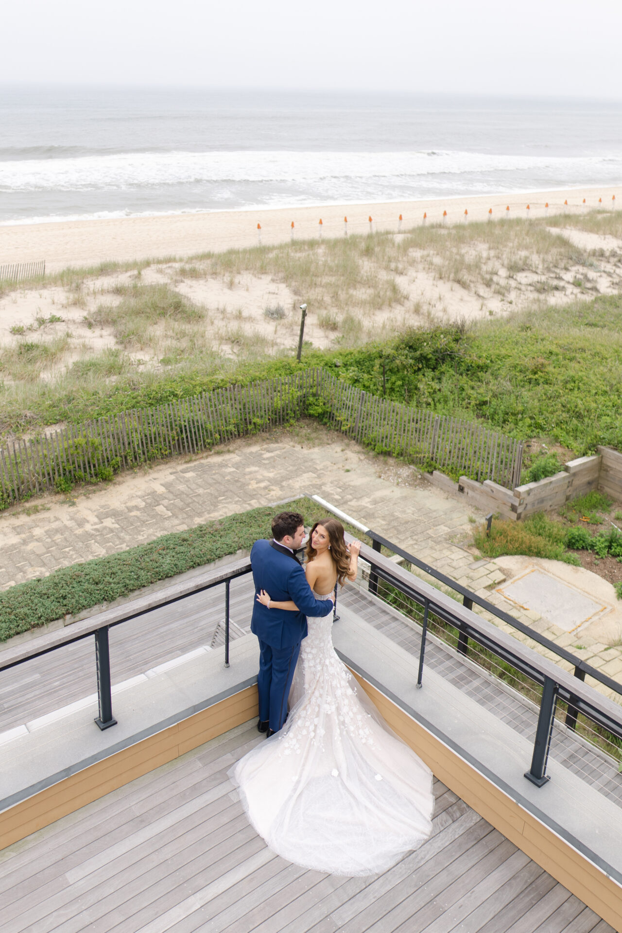 Bride and groom embrace on beachside wooden deck.
