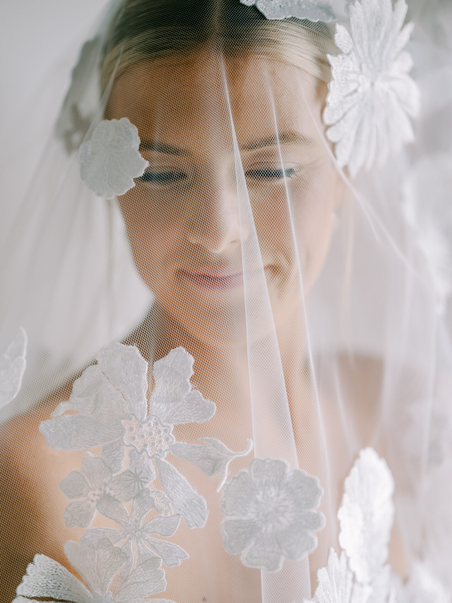 Blonde bride smiles under floral embroidered veil.