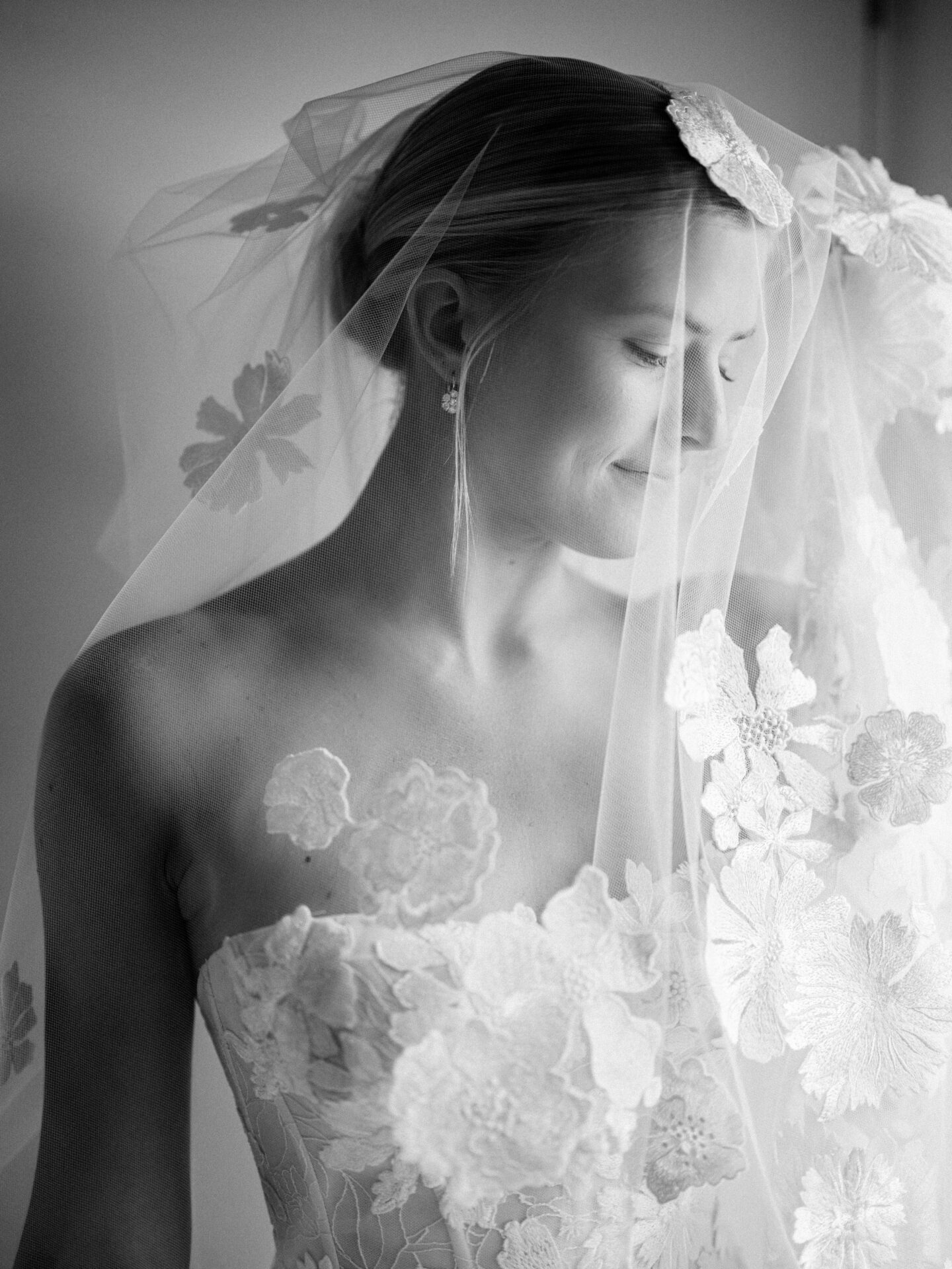 Bride in lace veil smiles peacefully, black-and-white.