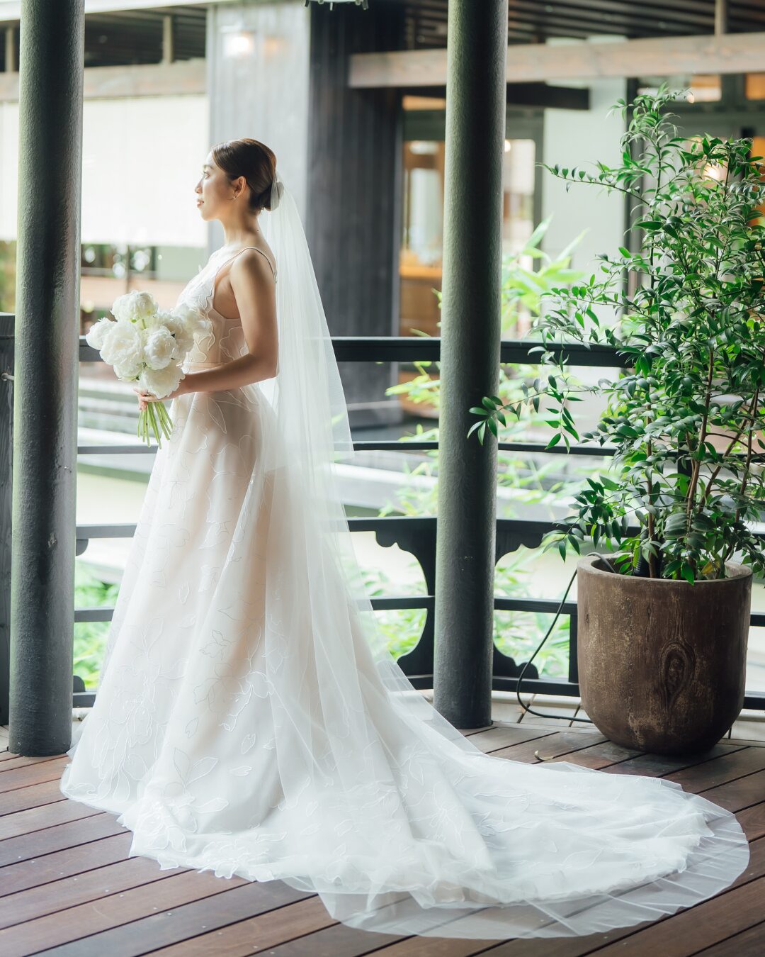 Bride in white dress holds bouquet indoors.