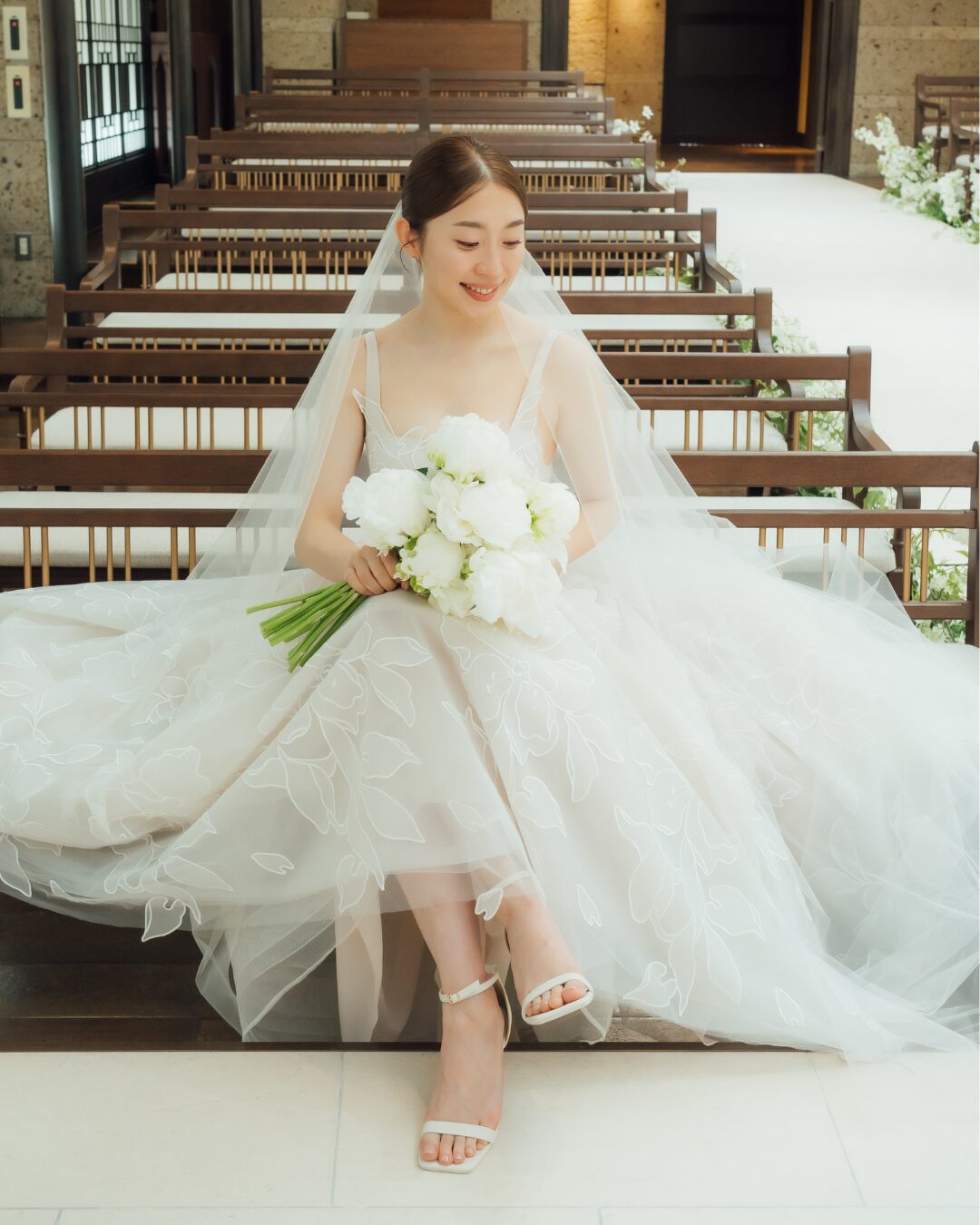 Bride in white dress smiling on bench.