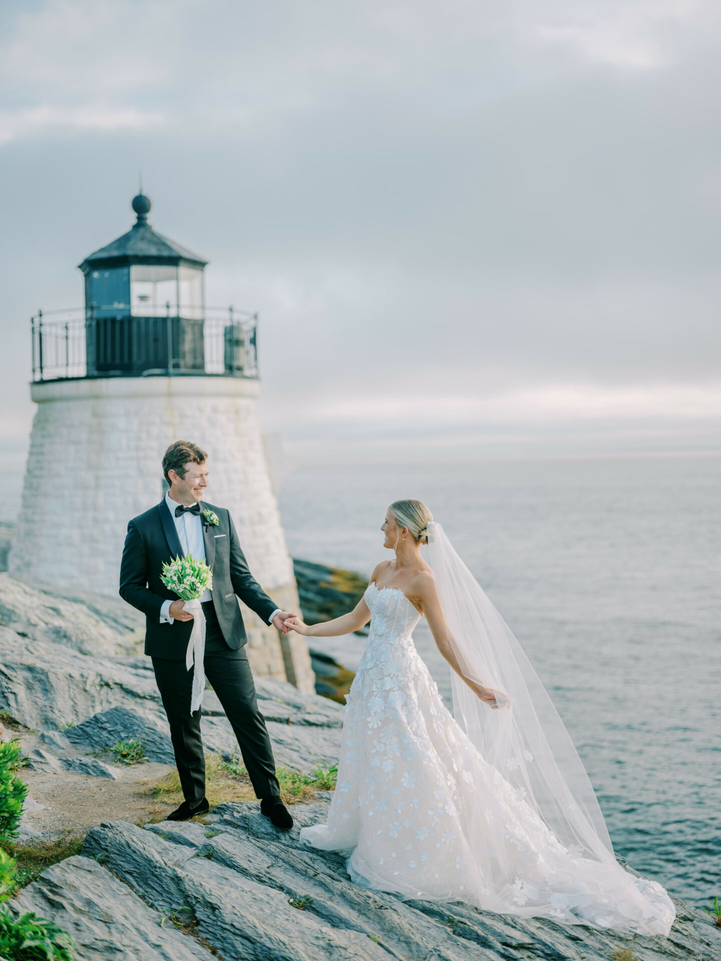 Bride and groom holding hands near lighthouse.